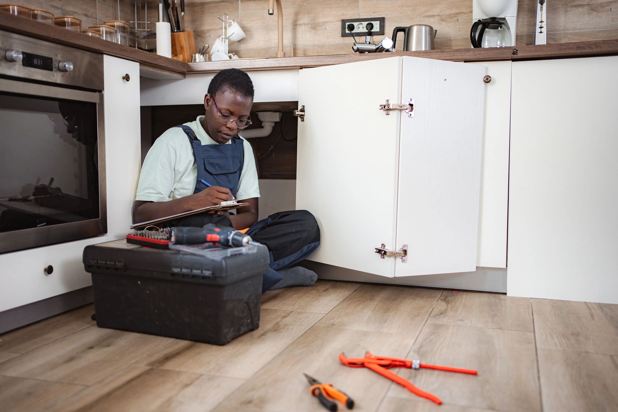 Plumber inspecting pipes under a kitchen sink during property maintenance